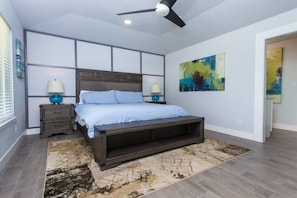 A bedroom with a bed, nightstands, a ceiling fan, and artwork on the walls.