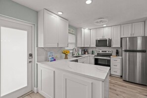 A modern kitchen with white cabinetry, a stainless steel refrigerator, a built-in oven, and a microwave.