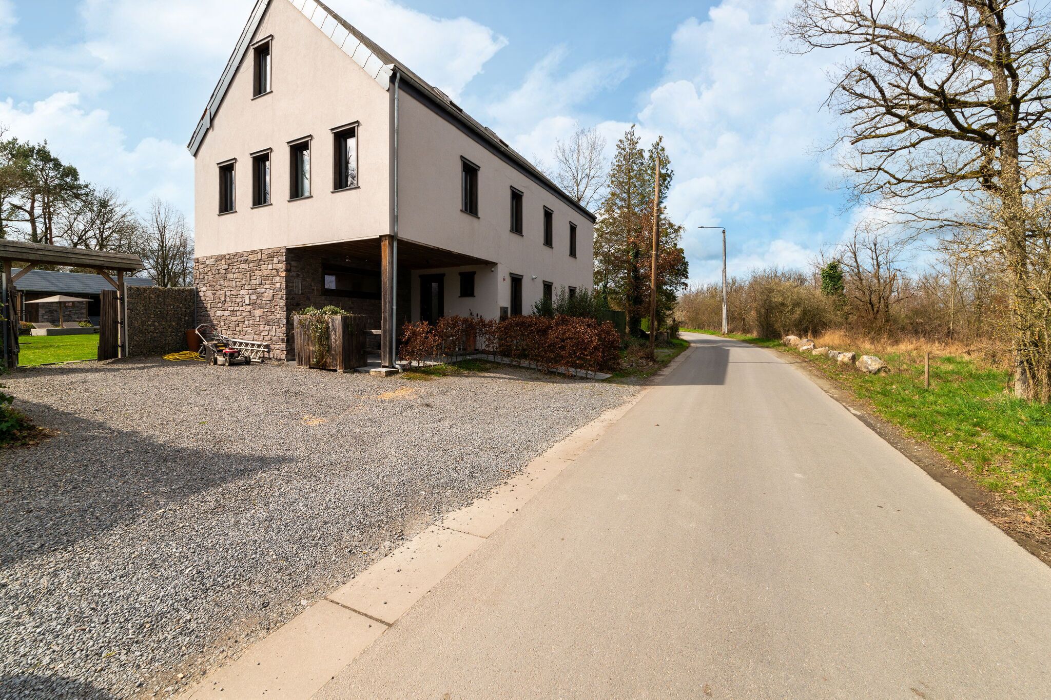 A modern two-story building with a stone base and a flat roof, located beside a paved road with a gravel driveway leading to the entrance.