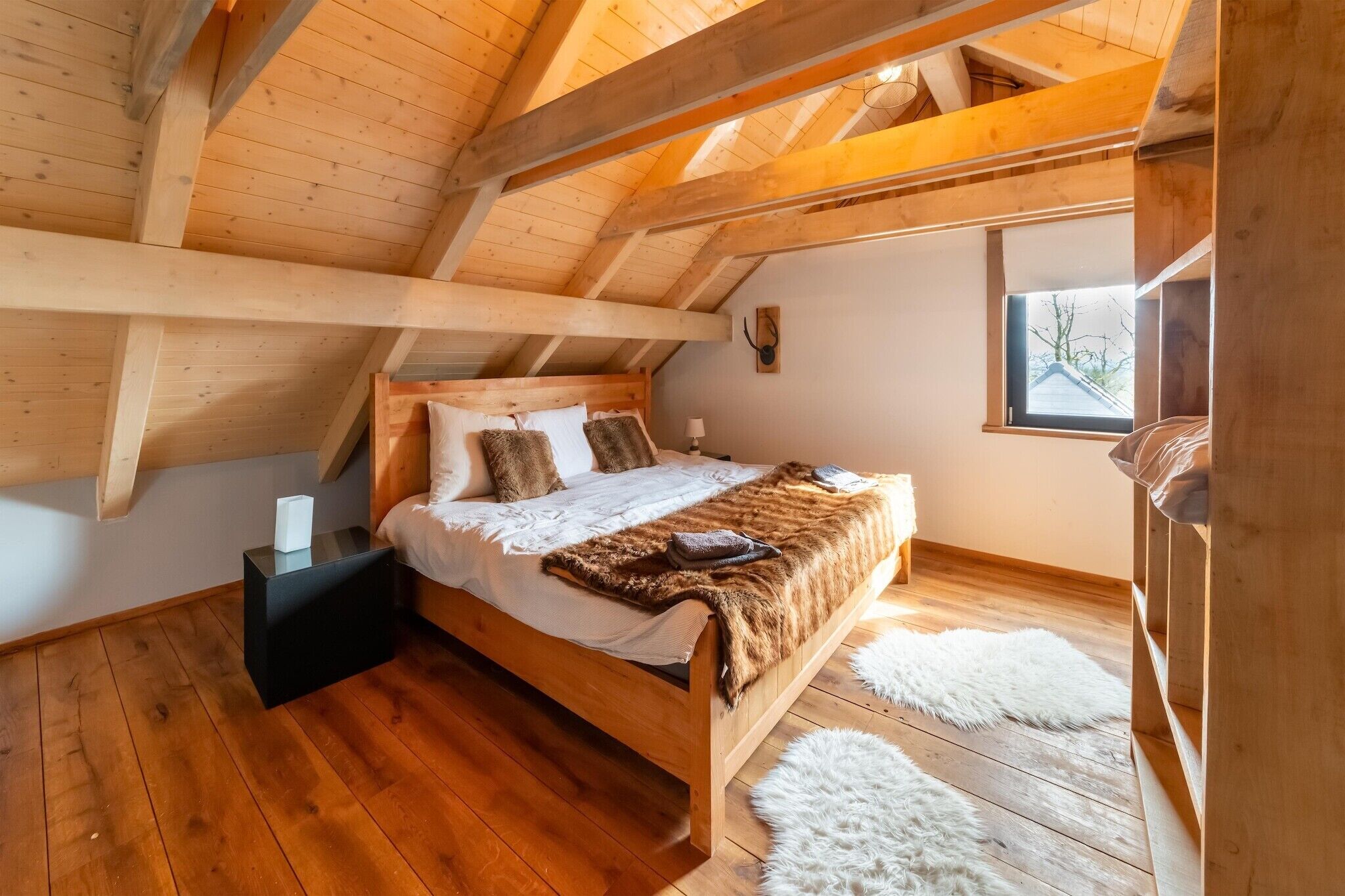 Une chambre mansardée avec une structure en bois, comprenant un lit, une table de chevet et une fenêtre.