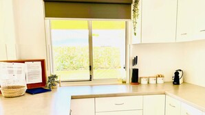 Una cocina con un ventanal grande, una cesta, una planta y un hervidor sobre la encimera.