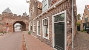A brick building with a large arched entrance, a black door, and a number 27 sign. - Beautiful and cozy monumental house in the city center. (Amersfoort)