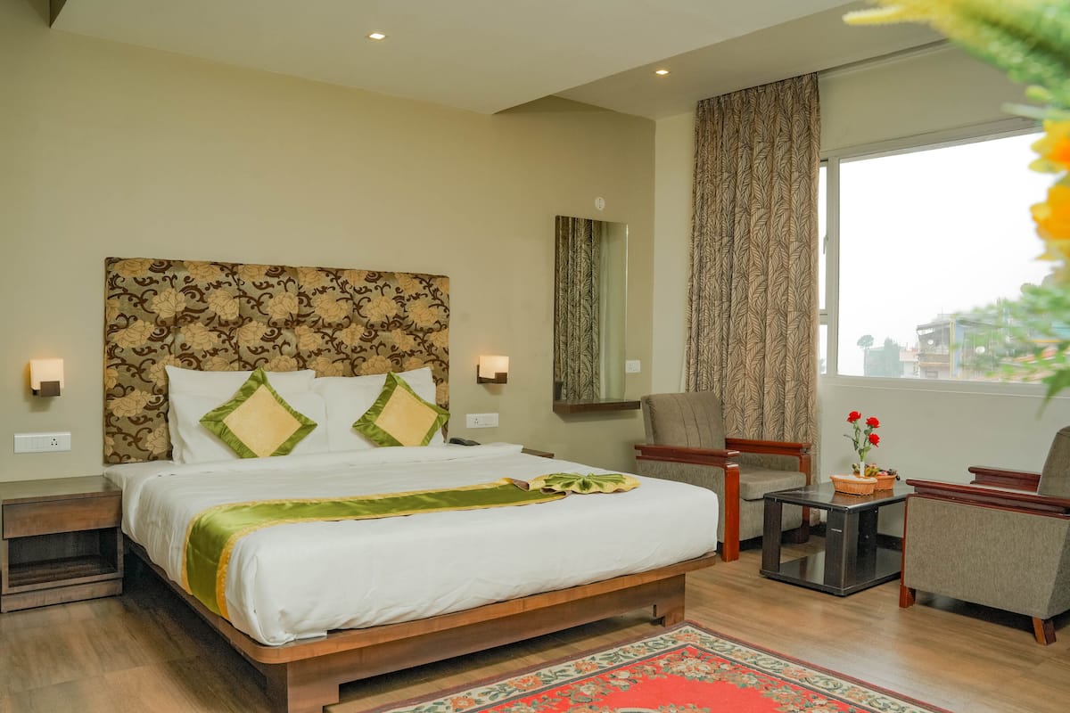 A hotel room with a large bed, a small table, a chair, and a view of the city through the window.