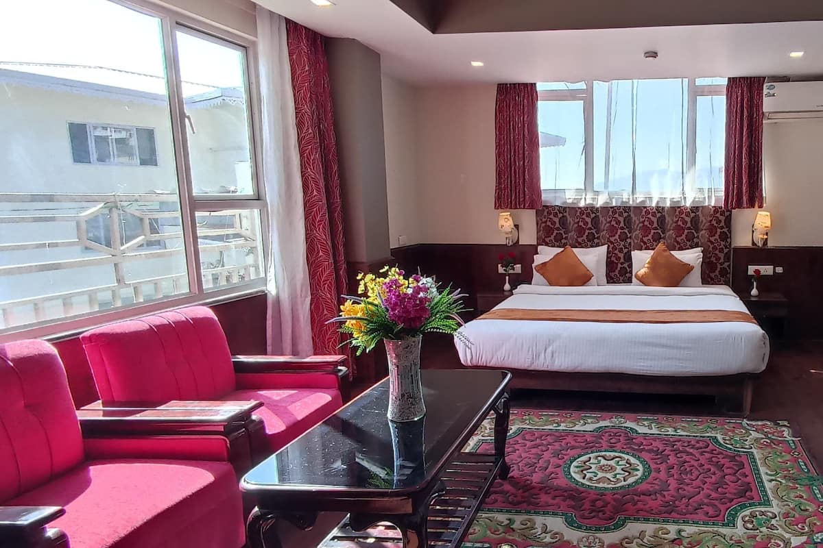 A hotel room with a bed, a desk, a chair, a sofa, a window, and an air conditioning unit.