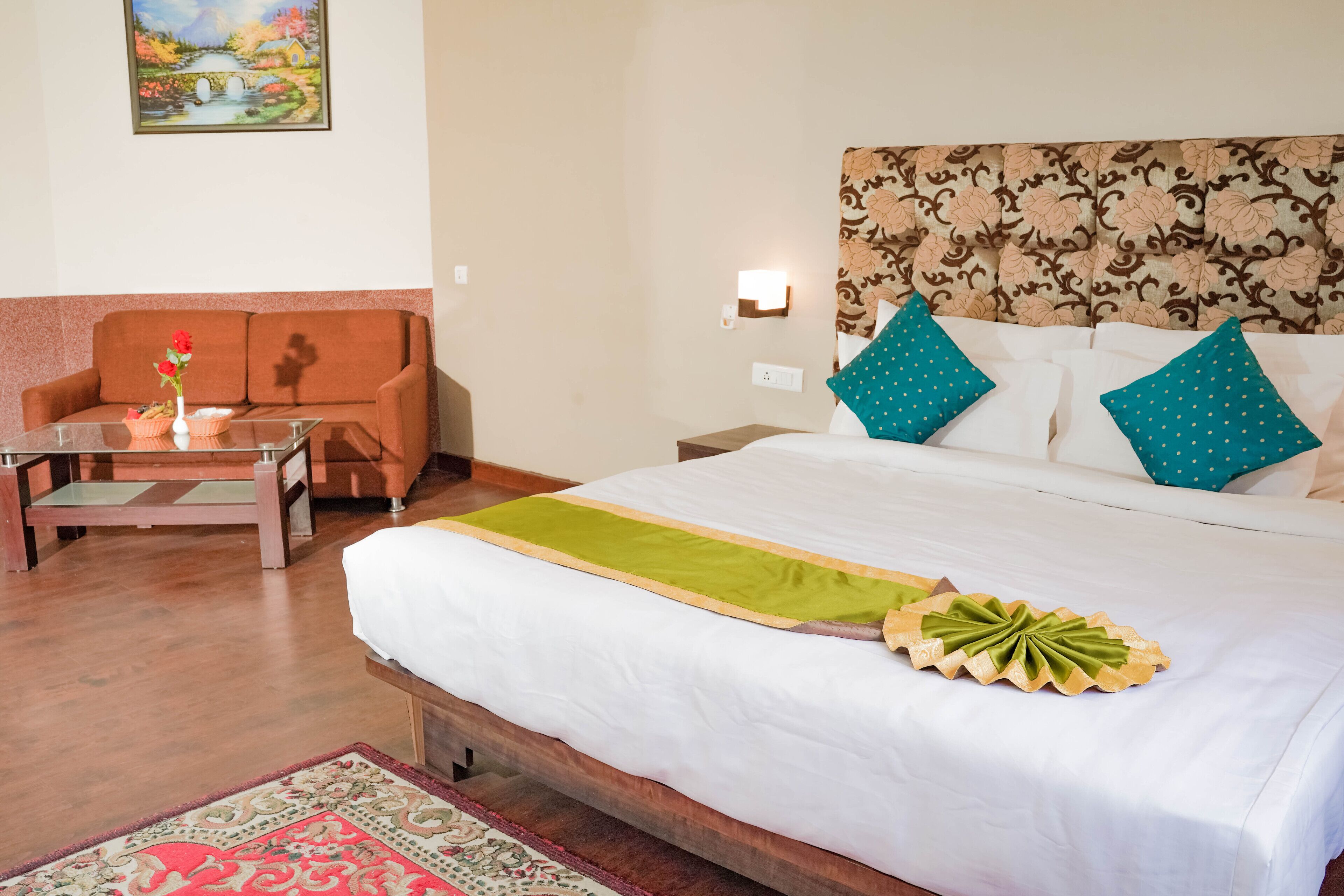 A hotel room with a bed, a sofa, a small table with a vase of flowers, and a painting on the wall.