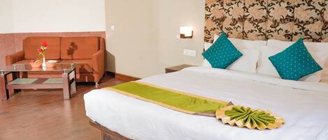 A hotel room with a bed, a sofa, a small table with a vase of flowers, and a painting on the wall.