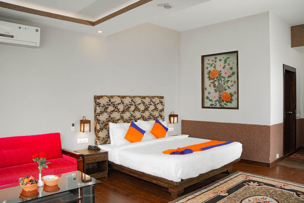 A hotel room with a bed, a red sofa, a small table with a vase and basket, and a wall-mounted air conditioner.