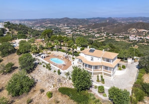 A large house with a swimming pool, surrounded by trees and hills.