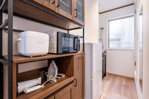 Et kompakt tekøkken med mikroovn, toaster og strygejern på hylder, samt et køleskab og et vindue med udsigt.