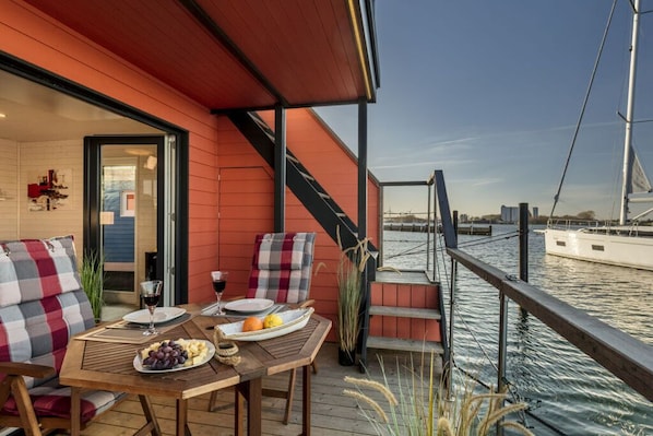 A wooden deck with a table set for two, overlooking a marina with boats.