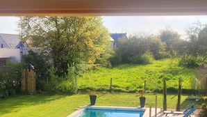 Una piscina rectangular con cubierta de madera y dos plantas en macetas, rodeada de un césped cuidado y una valla de madera.