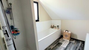 Un baño moderno con ducha, bañera y retrete. Hay una ventana que proporciona luz natural y un tendedero con algunas toallas.