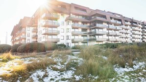 Un immeuble résidentiel à plusieurs étages, doté de balcons, entouré de pelouses et de quelques zones enneigées.