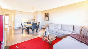 Un salon moderne avec une table basse en verre, un canapé gris et un tapis rouge.
