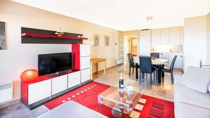 Un salon moderne avec un téléviseur à écran plat, une table basse en verre et un mur d’accent rouge.