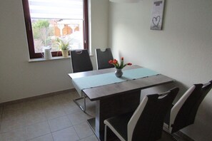 A small, private dining area with a table and four chairs, a window with plants, and a wall-mounted heart-shaped decoration.