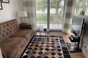 Un salon avec un canapé marron, une petite table ronde, un téléviseur et un tapis à motifs.
