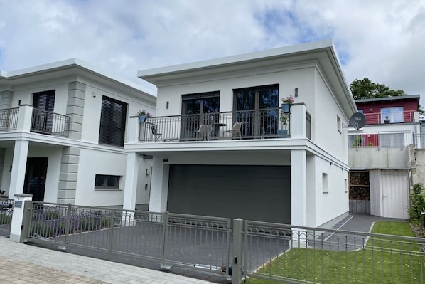 Une maison moderne à deux étages, dotée d’un garage, d’un balcon avec mobilier d’extérieur et d’une pelouse bien entretenue.