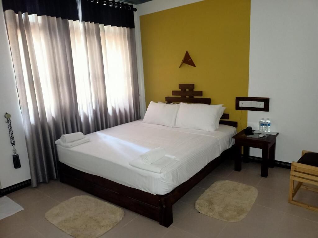 Una cama bien tendida con sábanas y almohadas blancas, un cabecero de madera, una mesita de noche con una botella de agua y una silla de madera.
