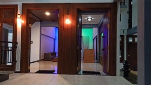 Un'ampia sala con porte in legno e pavimento piastrellato, che conduce a una stanza con una parete illuminata di verde.