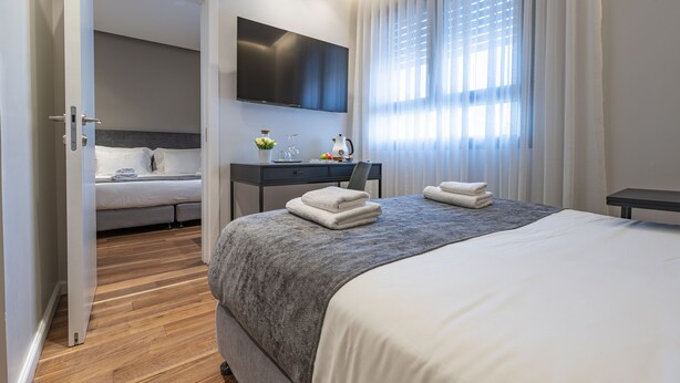 Habitación de hotel moderna con una cama grande, un escritorio, un televisor de pantalla plana y un baño visible a través de una puerta abierta.