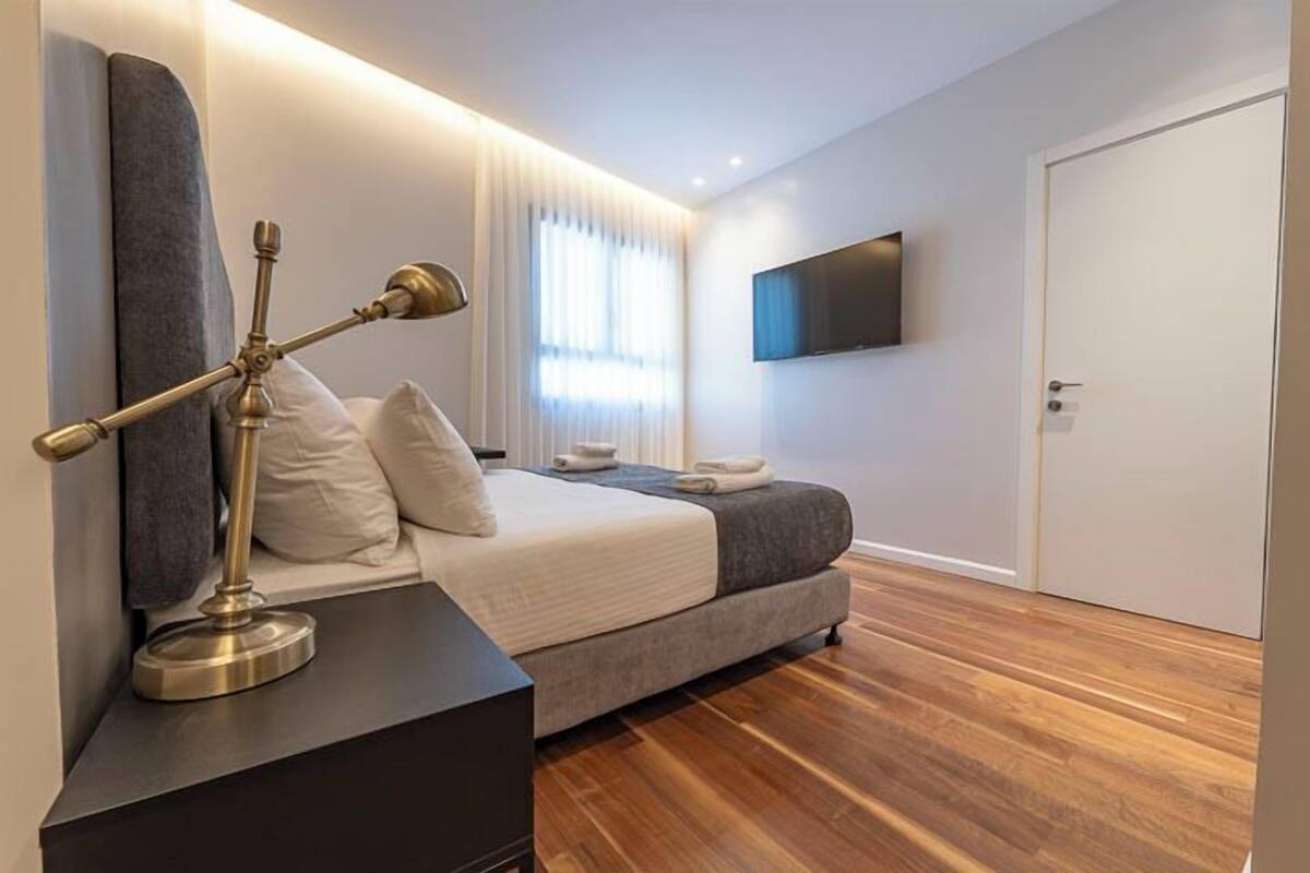 Ein modernes Schlafzimmer mit Bett, Nachttisch, Lampe und einem an der Wand befestigten Fernseher.