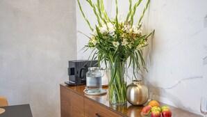 Un mueble de madera con un jarrón de flores, un frasco de vidrio, un cuenco de metal y un plato de manzanas y naranjas sobre una encimera de mármol.