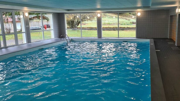 Piscina interna con pareti in vetro trasparente, pavimento piastrellato e vista su una zona verde esterna.