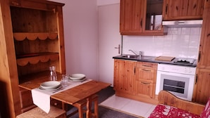 Una cucina compatta con mobili in legno, piano cottura integrato e zona pranzo con tavolo e sedie in legno.
