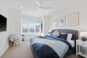 Ein modernes Schlafzimmer mit einem großen Bett, einem Deckenventilator und einem Fenster mit Jalousien.