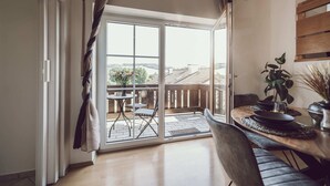 Une chambre moderne dotée d’une porte-fenêtre coulissante donnant sur un balcon, d’un coin repas avec une table et des chaises, et d’une plante en pot.