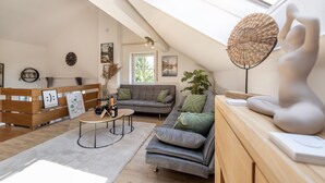 Un loft moderne avec un plafond en pente, un canapé gris, un banc en bois et une grande sculpture abstraite.