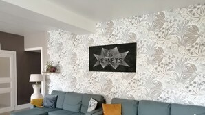 Ett modernt vardagsrum med en turkos soffa, ett svart konstverk på väggen och en mönstrad tapet.