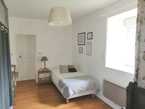 Un dormitorio pequeño y bien iluminado con una cama individual, una lámpara de noche y una ventana con cortinas.