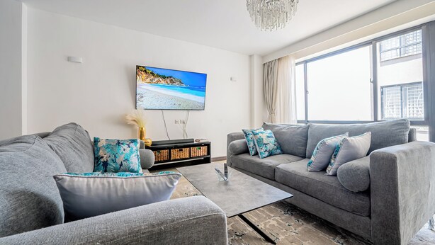 A modern living room with grey sofas, a coffee table, and a large window with curtains. - Rose Upscale Apt (Nairobi)