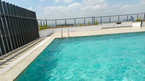 A rooftop swimming pool with clear blue water, a tiled deck, and a city skyline in the background. - Rose Upscale Apt (Nairobi)