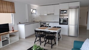 Una cocina moderna con armarios blancos, horno empotrado y comedor con mesa y sillas.