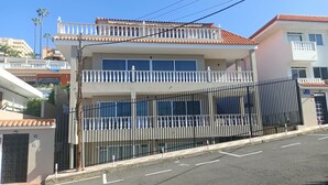 Un edificio de dos plantas con balcón, entrada protegida por un portón y cielo despejado.