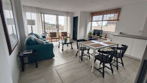 Una sala de estar con sofá, una mesa de comedor con sillas, televisor y ventana con persianas.