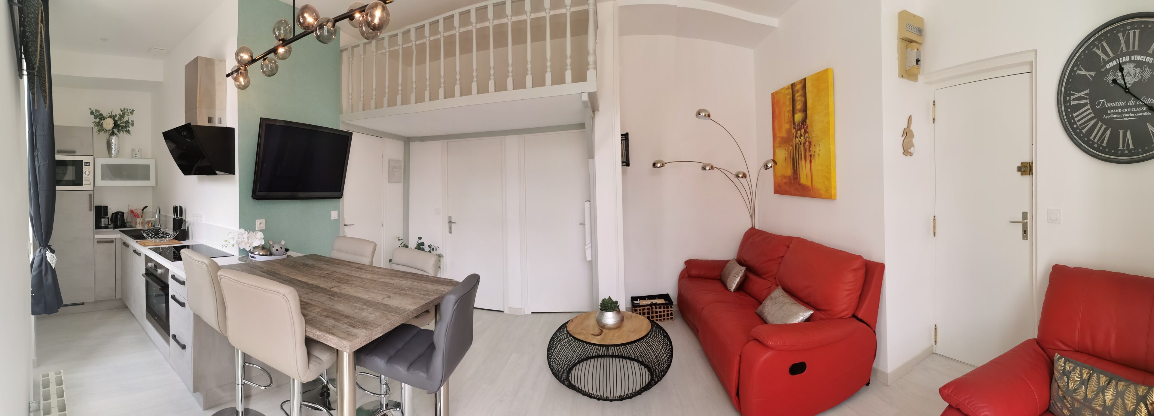 Una cocina moderna con zona de comedor, un sofá rojo y un reloj de pared.