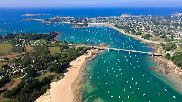 An aerial view of a coastal area with a bridge, boats, and a beach.