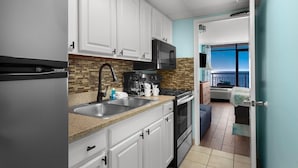 A compact kitchen with white cabinets, a microwave, a coffee maker, and a sink.