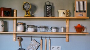 Une cuisine avec des étagères en bois où sont rangés les ustensiles de cuisine, un porte-ustensiles suspendu et une machine à café.