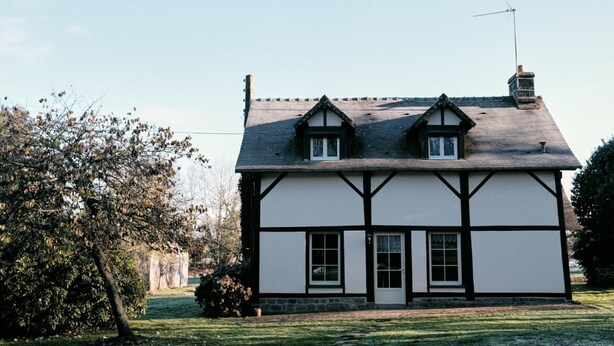 Une maison traditionnelle à colombages, avec un toit en pente, une cheminée et une antenne visible.