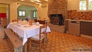 Un coin repas agrémenté d’une cheminée en pierre, une cuisine équipée d’un lave-vaisselle et une table à manger pour quatre personnes.
