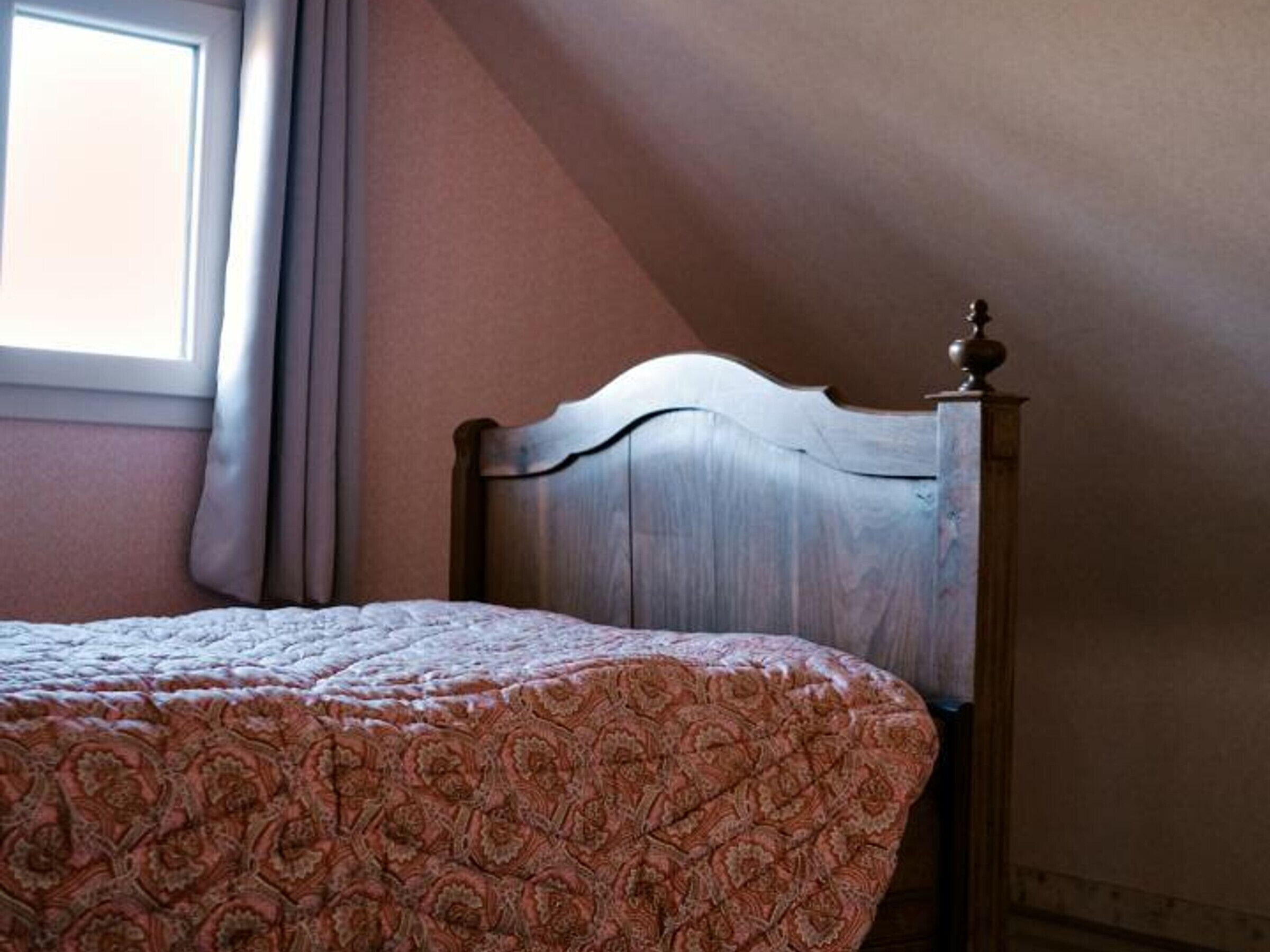 A bedroom with a bed, a wooden headboard, and a window with curtains.