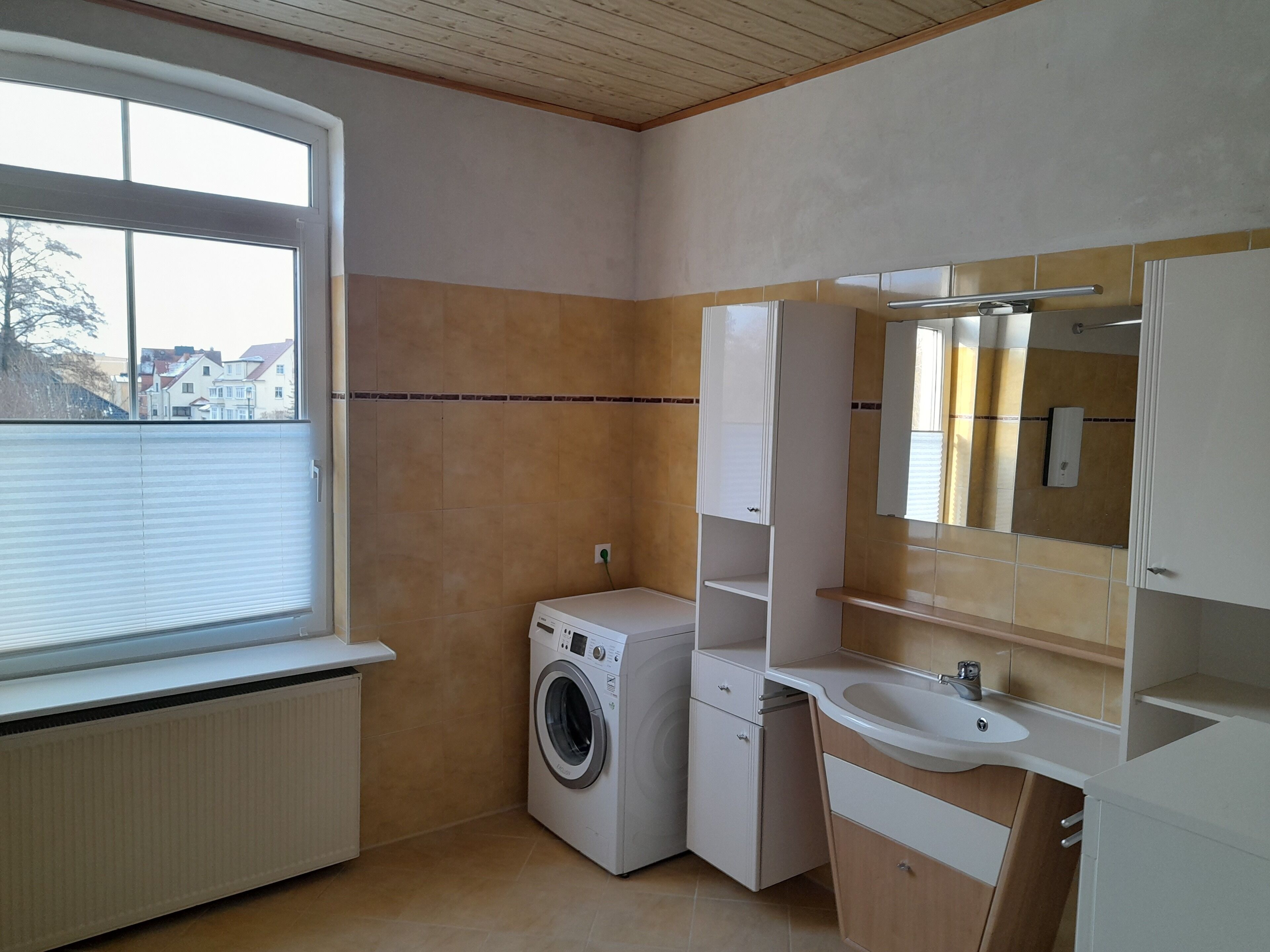 A compact, modern bathroom with a built-in washing machine, a sink, and a mirror.