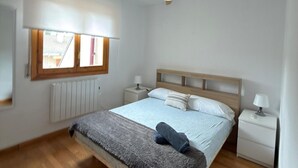 Makuuhuone, jossa on sänky, kattotuuletin, ikkuna, patteri ja yöpöydät.