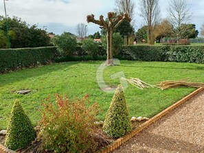 Un jardin bien entretenu, avec une pelouse soigneusement taillée, une variété d’arbustes et un arbre central à la forme particulière.