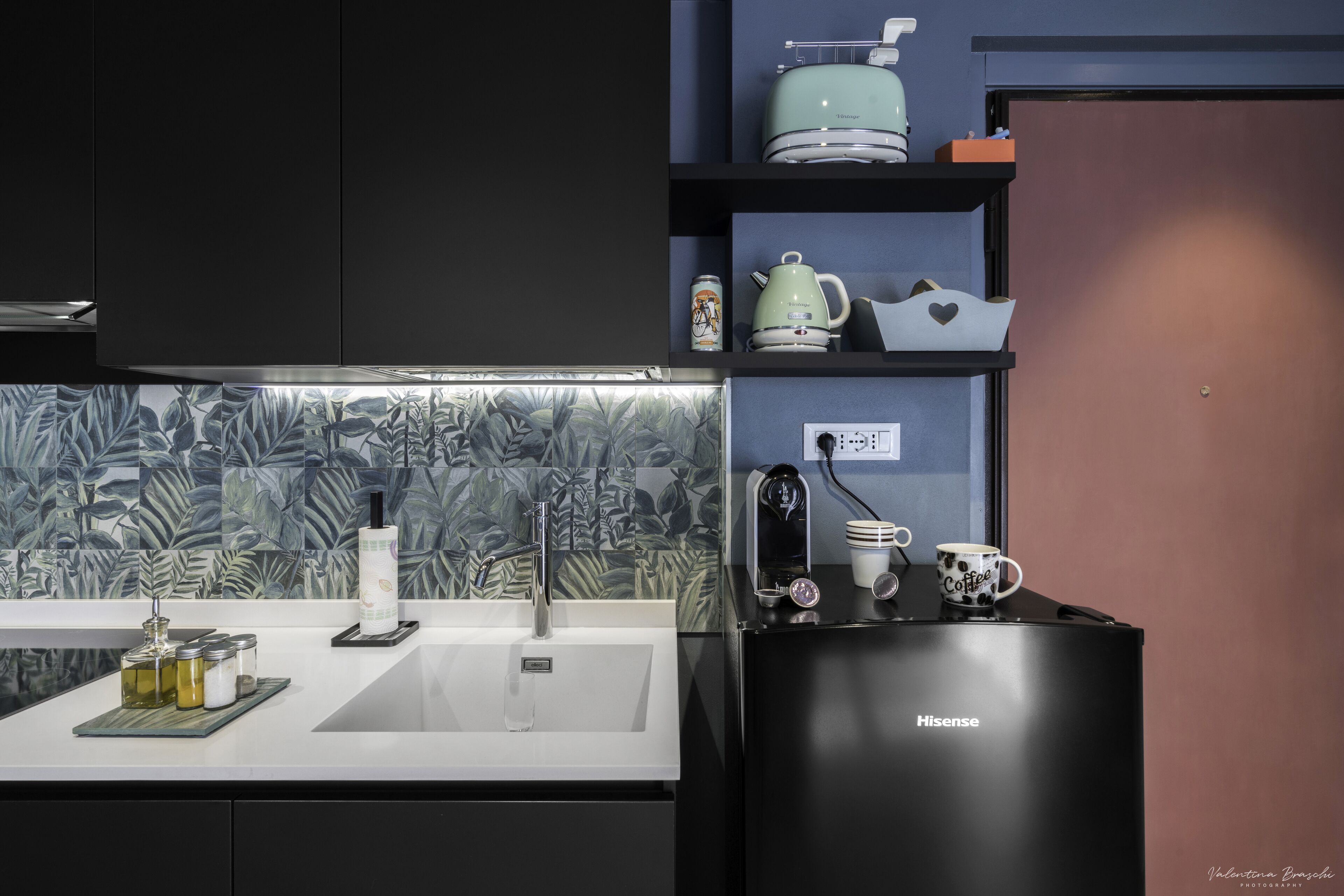 A modern kitchen with a black refrigerator, a white sink, and a backsplash with a leaf pattern.